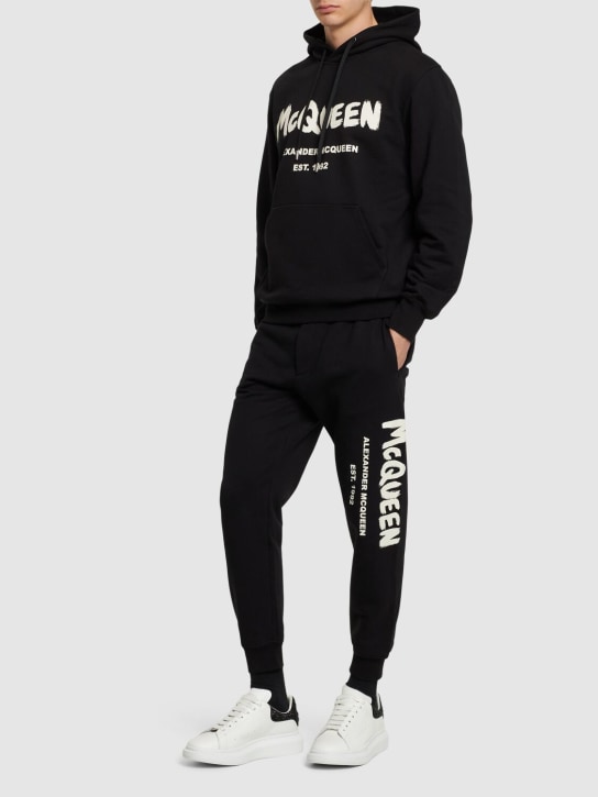 Alexander McQueen: Pantaloni in felpa di cotone con logo - Nero/Avorio - men_1 | Luisa Via Roma